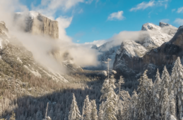 A breathtaking winter landscape of Yosemite National Park with snow-covered trees and cliffs partially obscured by clouds.