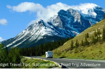 A scenic view of a highway leading through a mountainous landscape with lush greenery and a clear blue sky. A recreational vehicle is seen traveling on the road, with towering snow-capped mountains in the background.